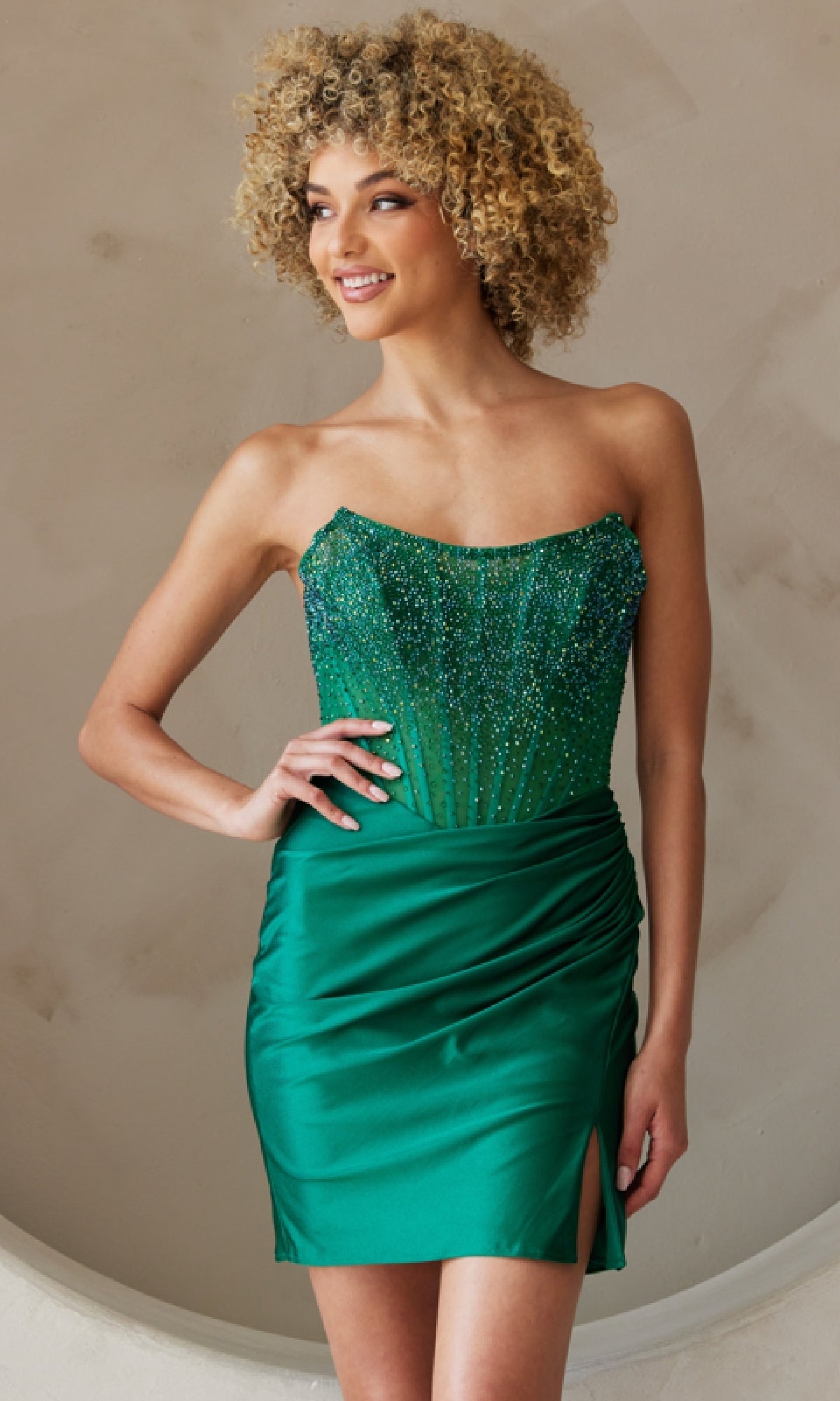 Woman wearing the Beaded-Bodice Strapless Short Hoco Dress 3021S, a fitted green dress with a beaded corset bodice and ruched satin skirt featuring a thigh-high slit.